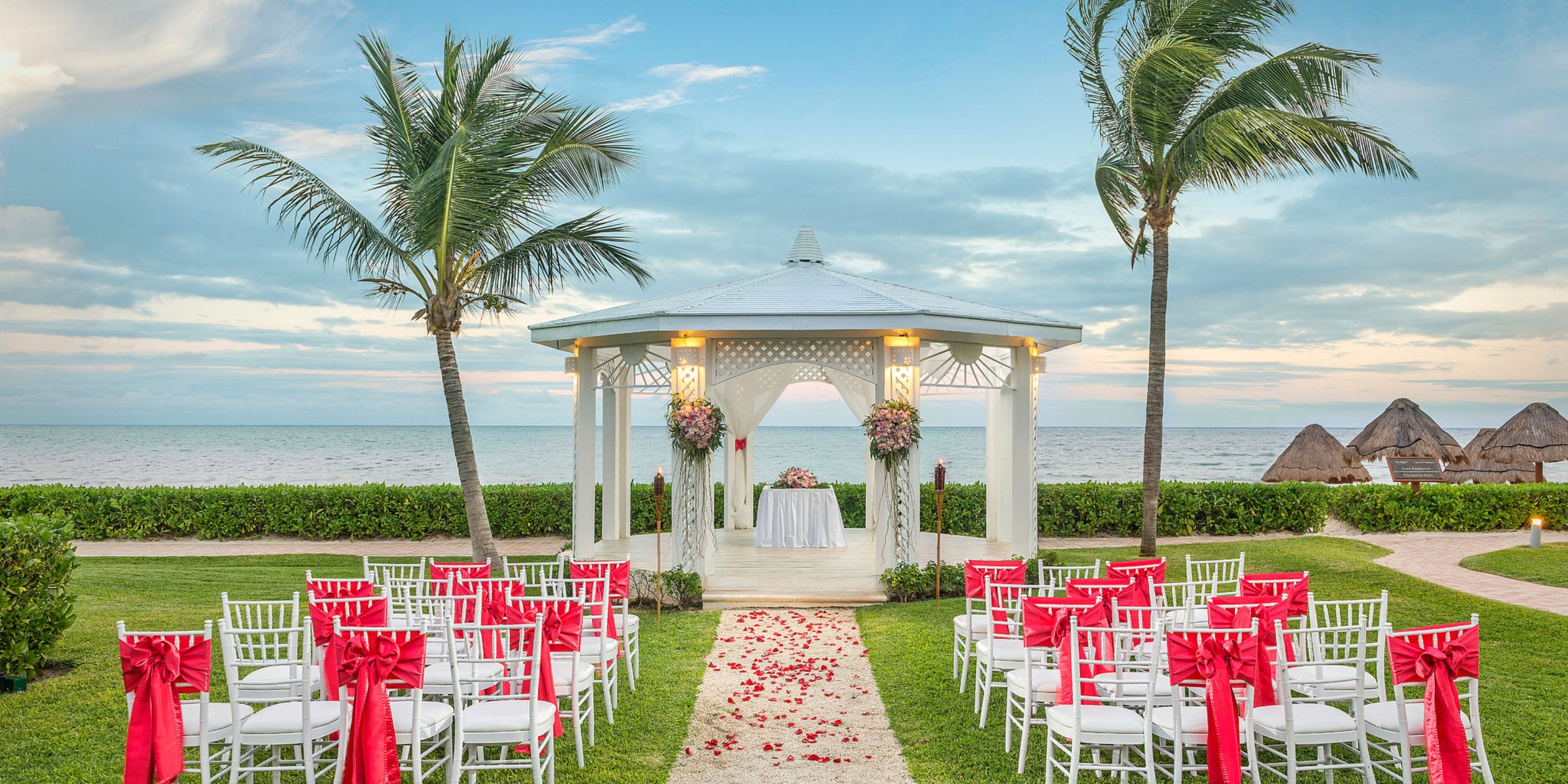 Destination wedding at Ocean Coral and Turquesa: white chairs with red ribbons by the oceanfront gazebo.