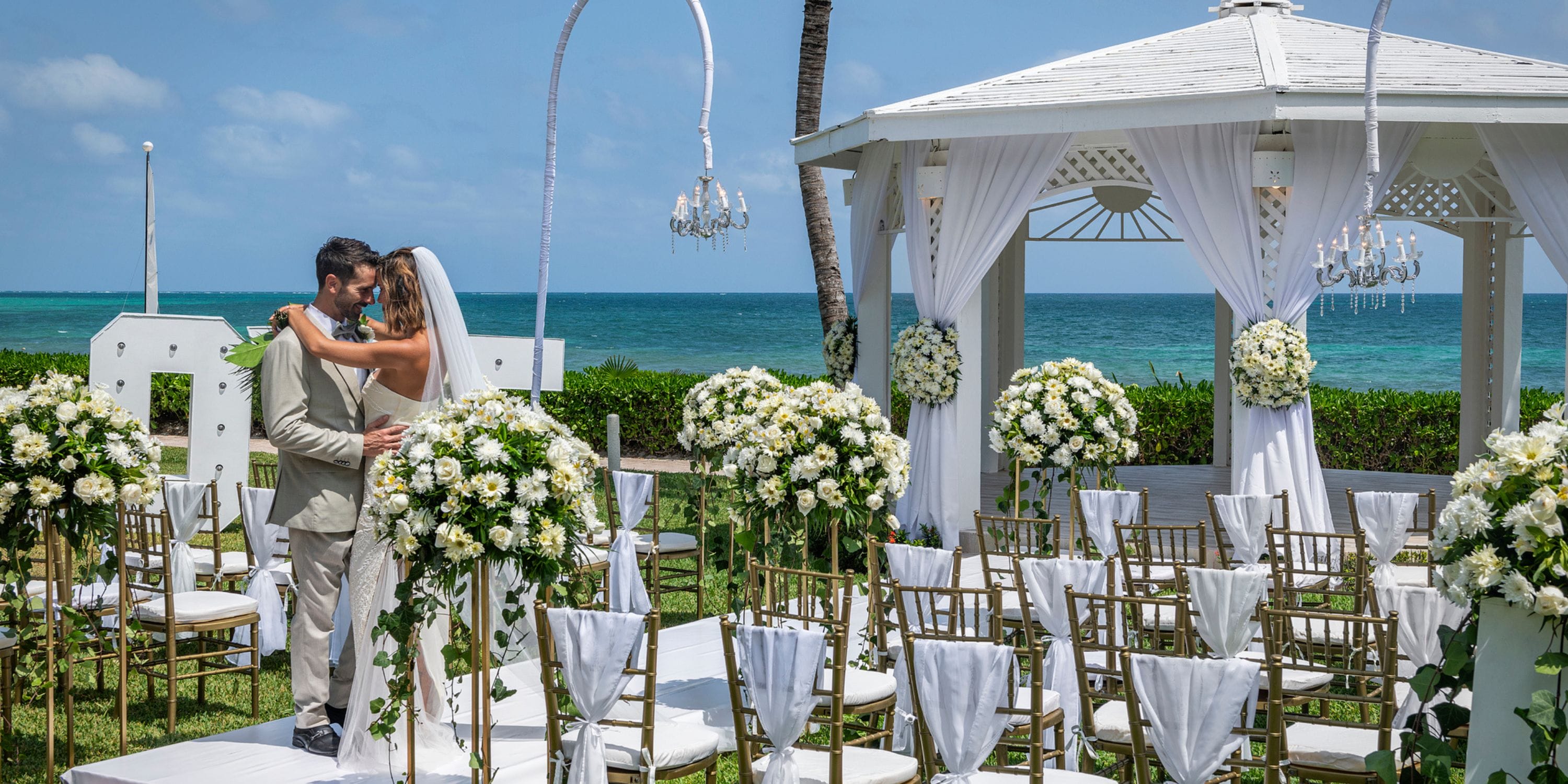 Bride and groom embrace at a destination wedding gazebo by the ocean at Ocean Coral and Turquesa.
