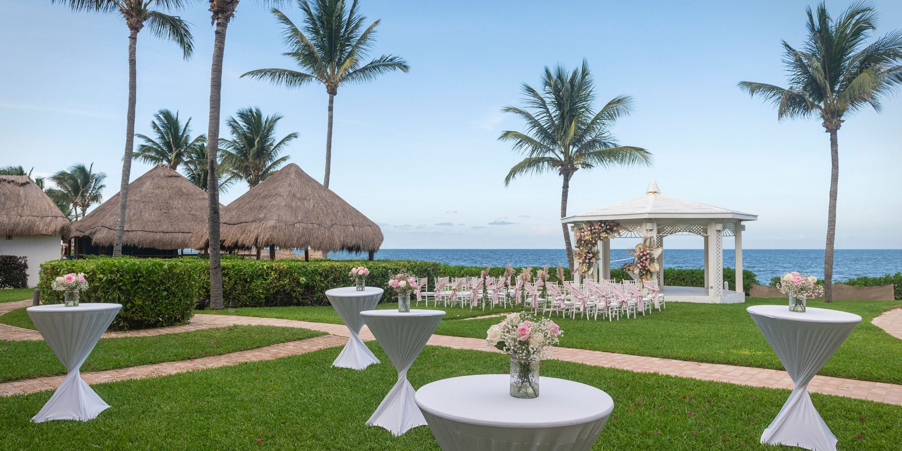 A destination wedding lawn at Ocean Coral and Turquesa, with palm trees, gazebos, and ocean views.