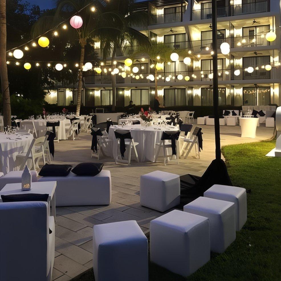 Destination wedding evening with round tables, white chairs, string lights, and stylish modern seating.