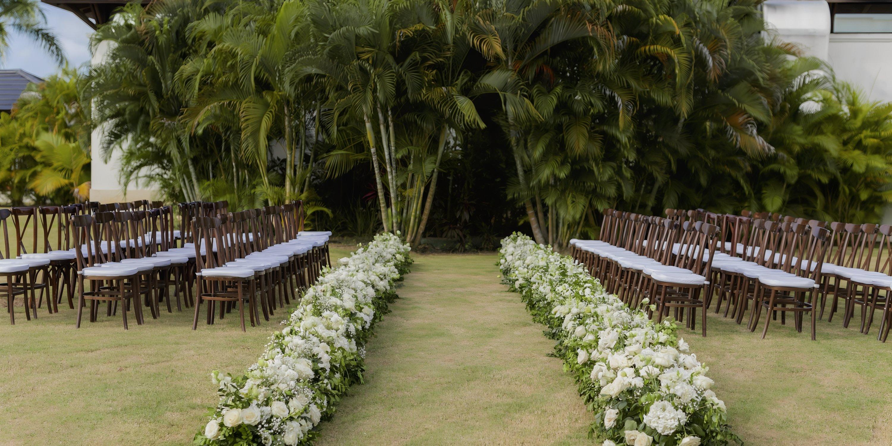Ocean El Faro destination wedding setup with rows of chairs and a flower-lined aisle on lush grass.