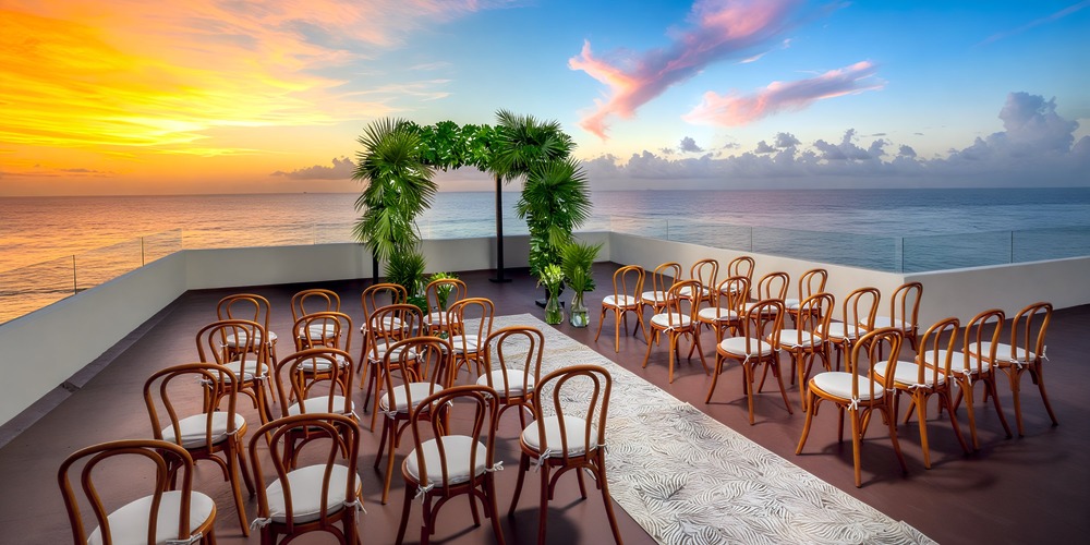 Sunset destination wedding setup on the rooftop, featuring elegant chairs and a stunning floral arch overlooking the ocean.