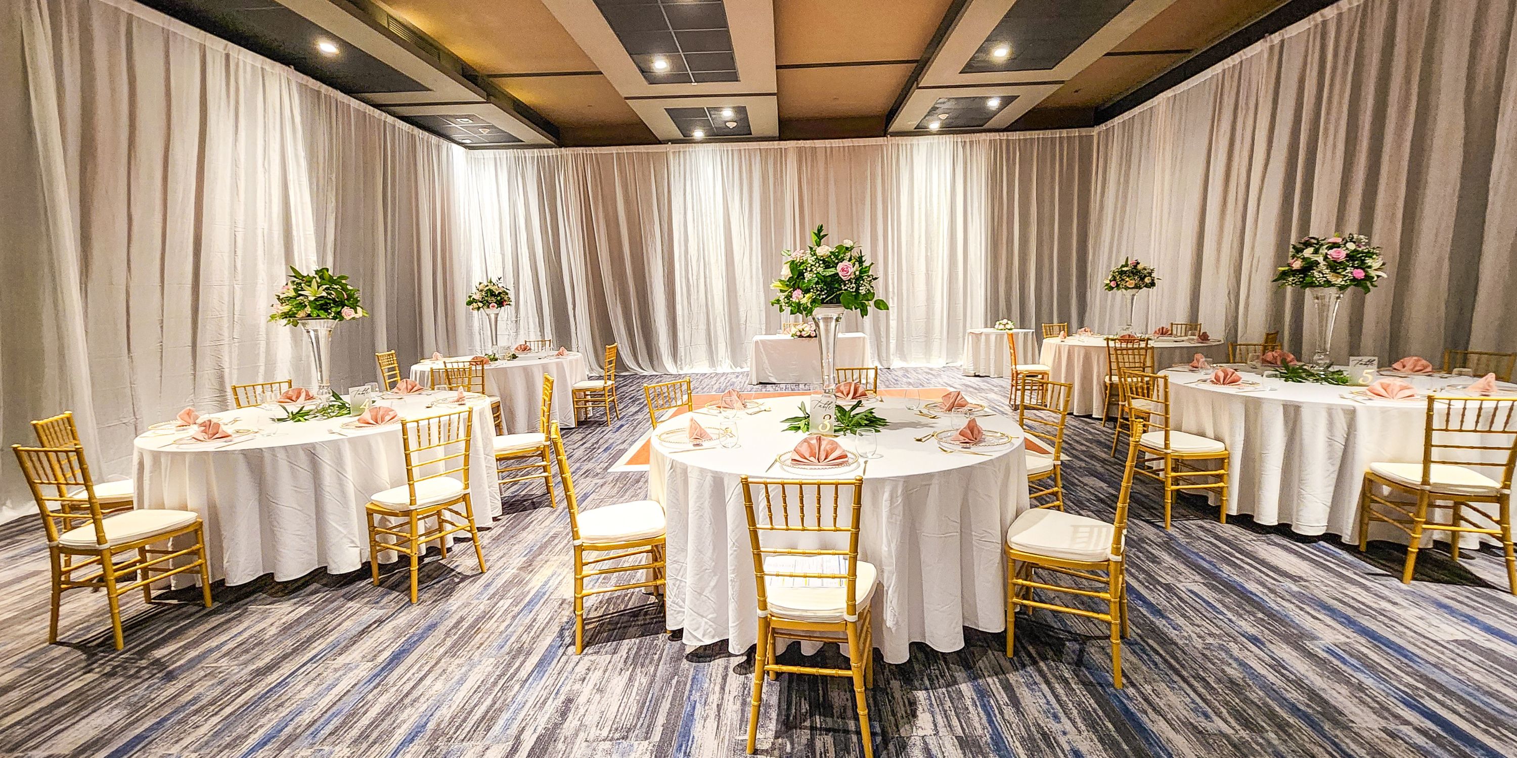 Royalton Antigua: Elegant wedding event hall with round tables, white linens, gold chairs, and florals.