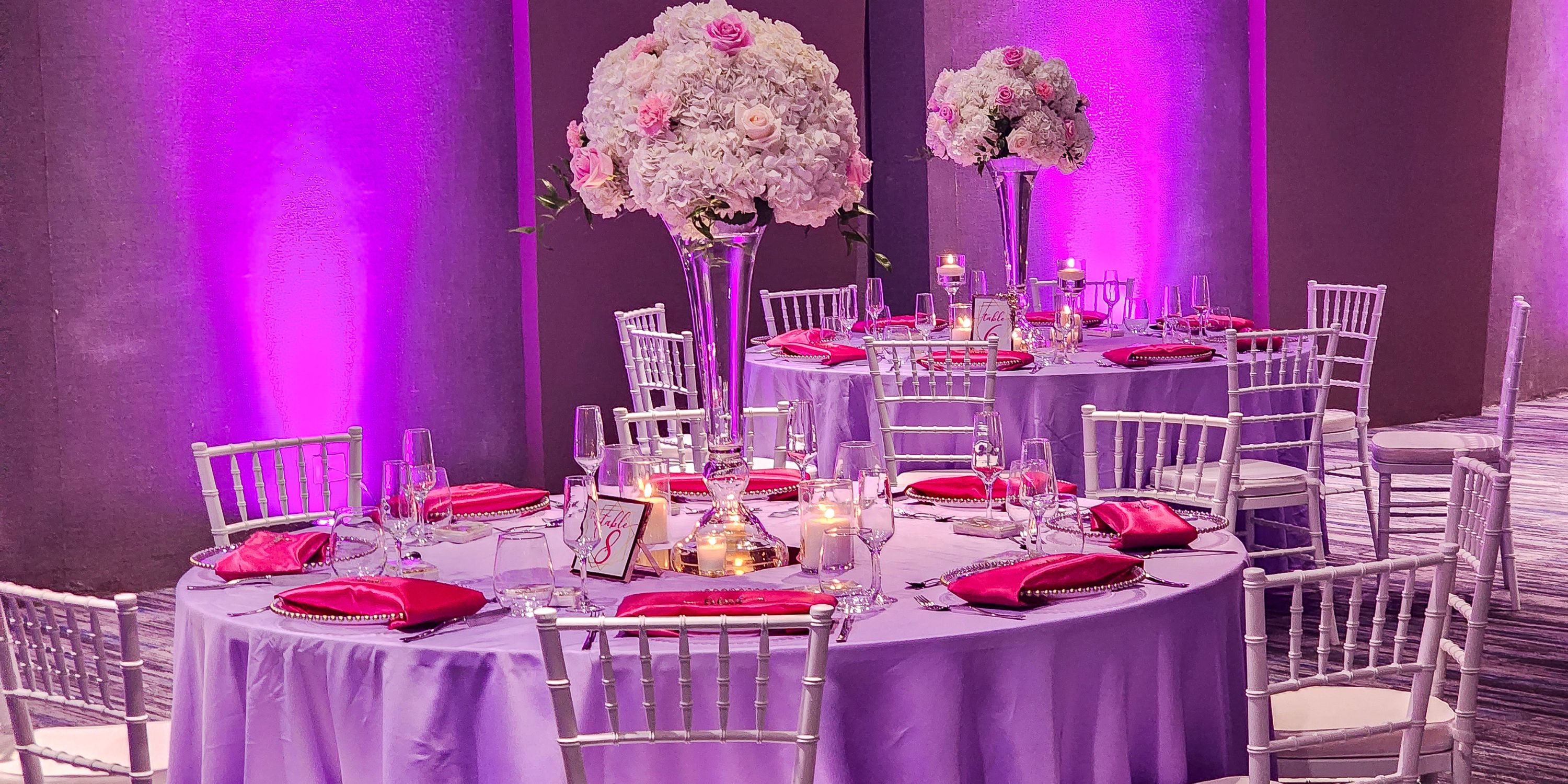 Royalton Antigua destination wedding setup with round tables, pink napkins, florals, and purple lighting.