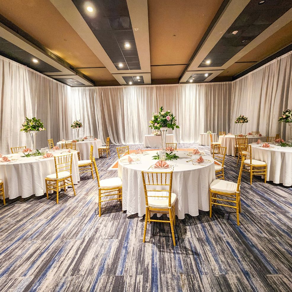 Elegant banquet hall set for a destination wedding, with round tables, white linens, gold chairs, and florals.