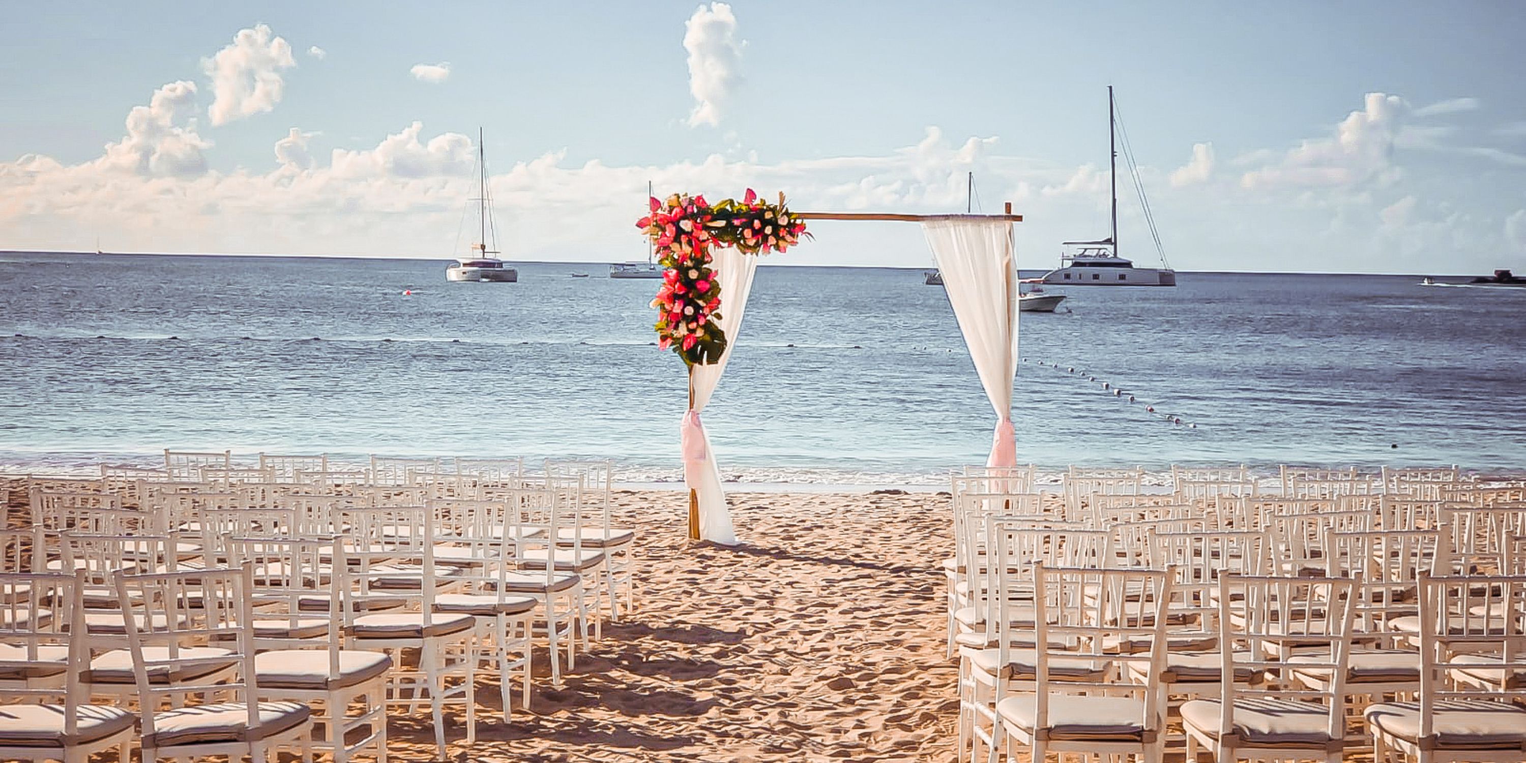 Destination wedding ceremony setup on the beach at Royalton Antigua with chairs and a floral arch.