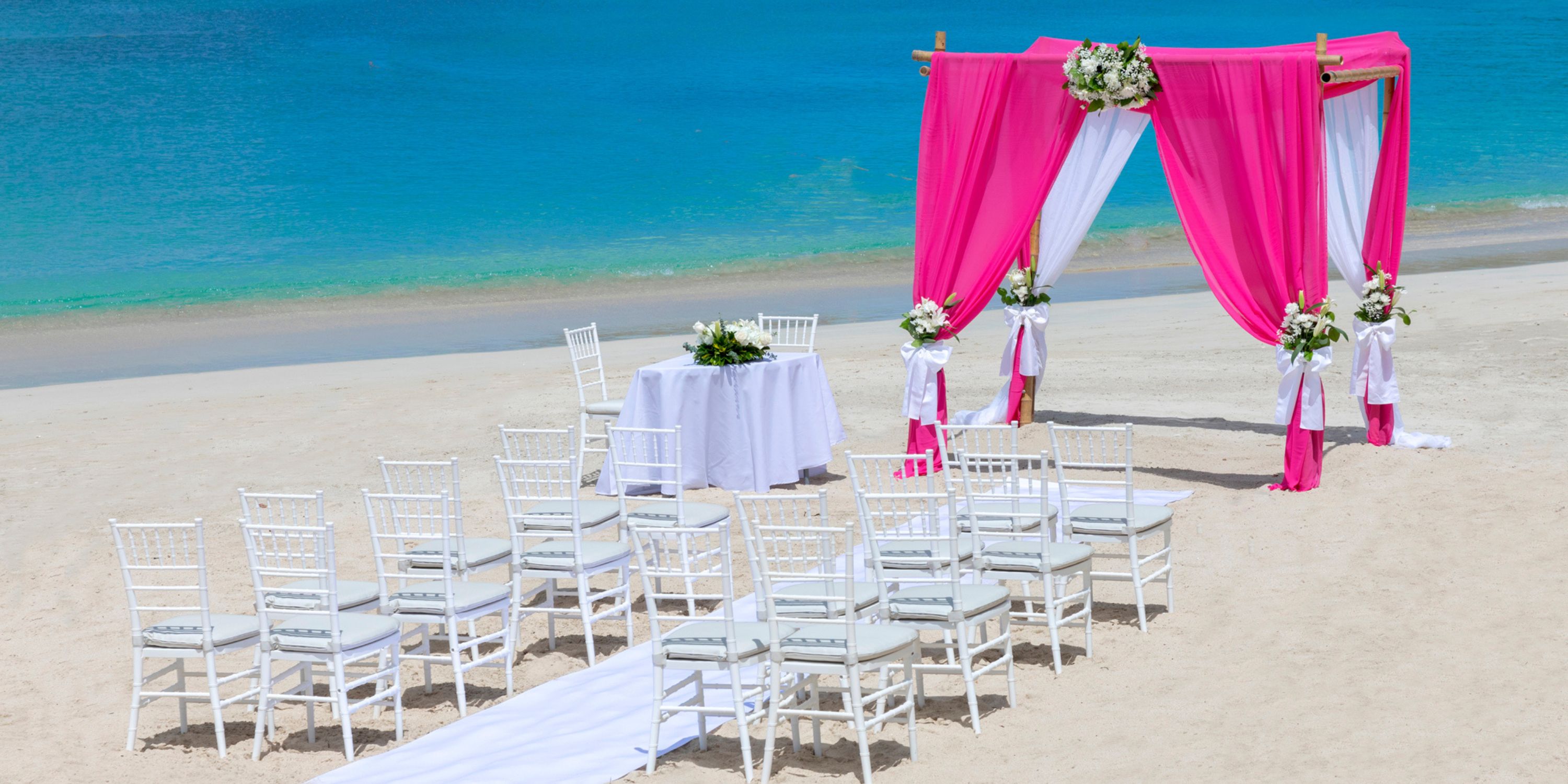 Destination wedding setup at Royalton Antigua with white chairs, pink drapes, and flowers by the ocean.