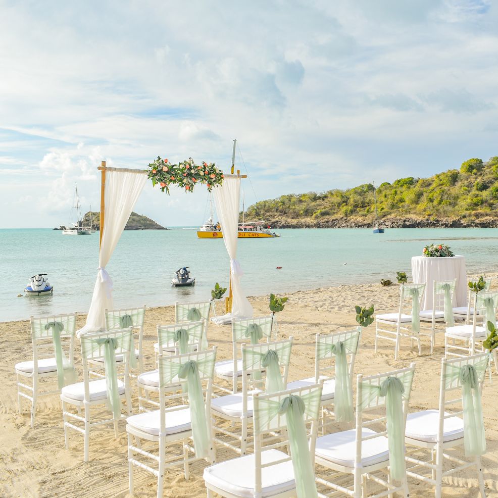 White chairs set up on the sand for a destination wedding ceremony, all facing toward the ocean.