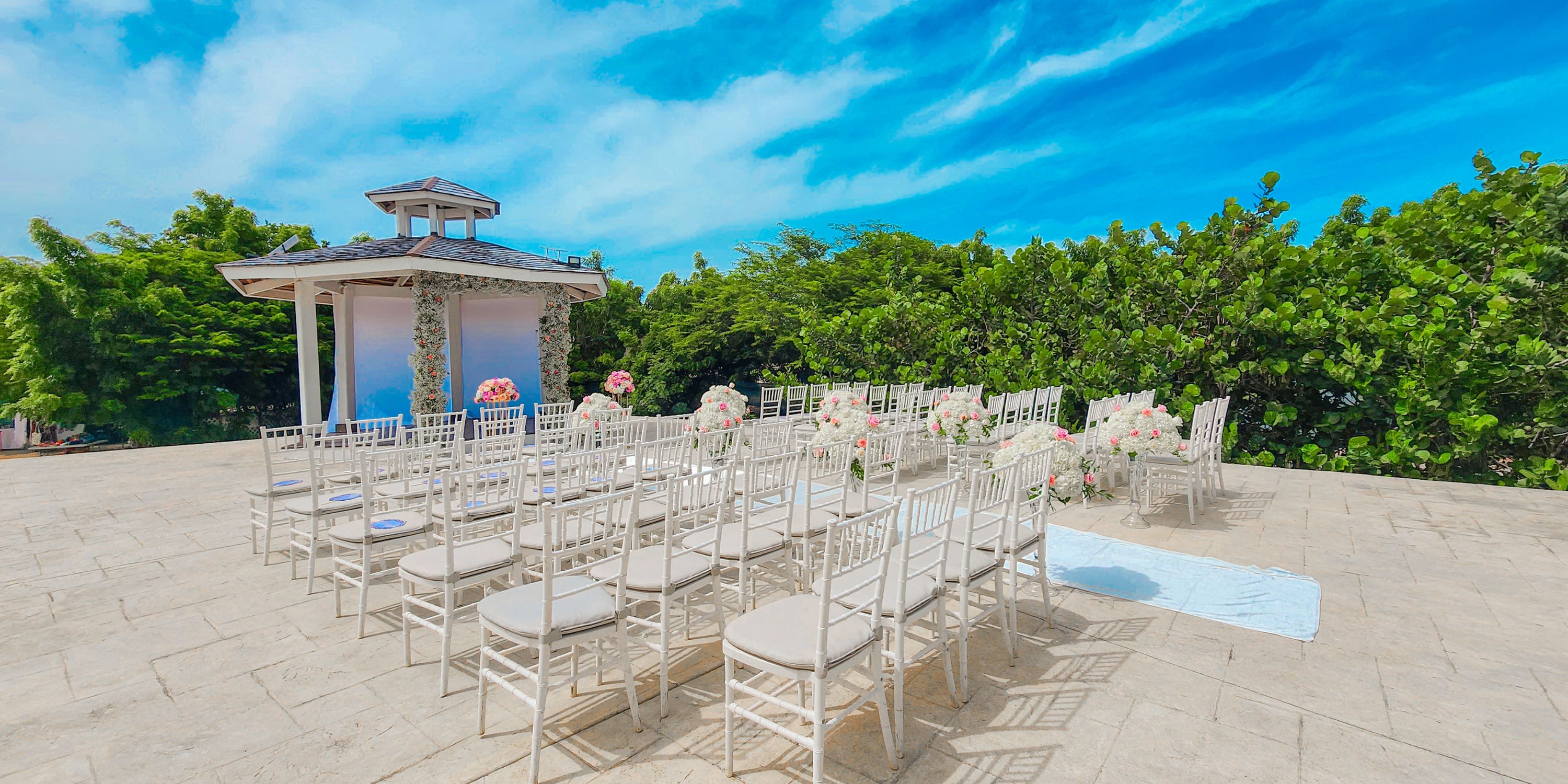 Destination wedding at Royalton Antigua: white chairs, florals, and a gazebo beneath a blue sky.