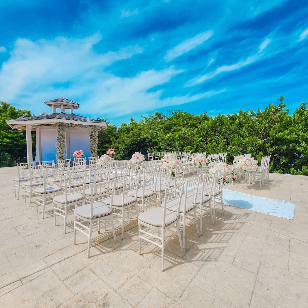 Destination wedding ceremony setup featuring white chairs, floral decor, and a charming gazebo outdoors.