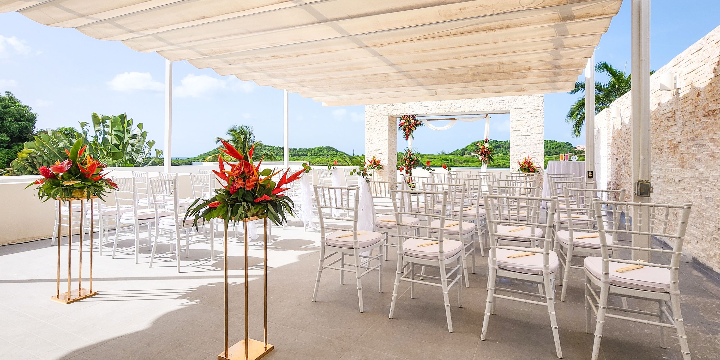 Destination wedding at Royalton Antigua with white chairs and red flowers set beneath an elegant canopy.