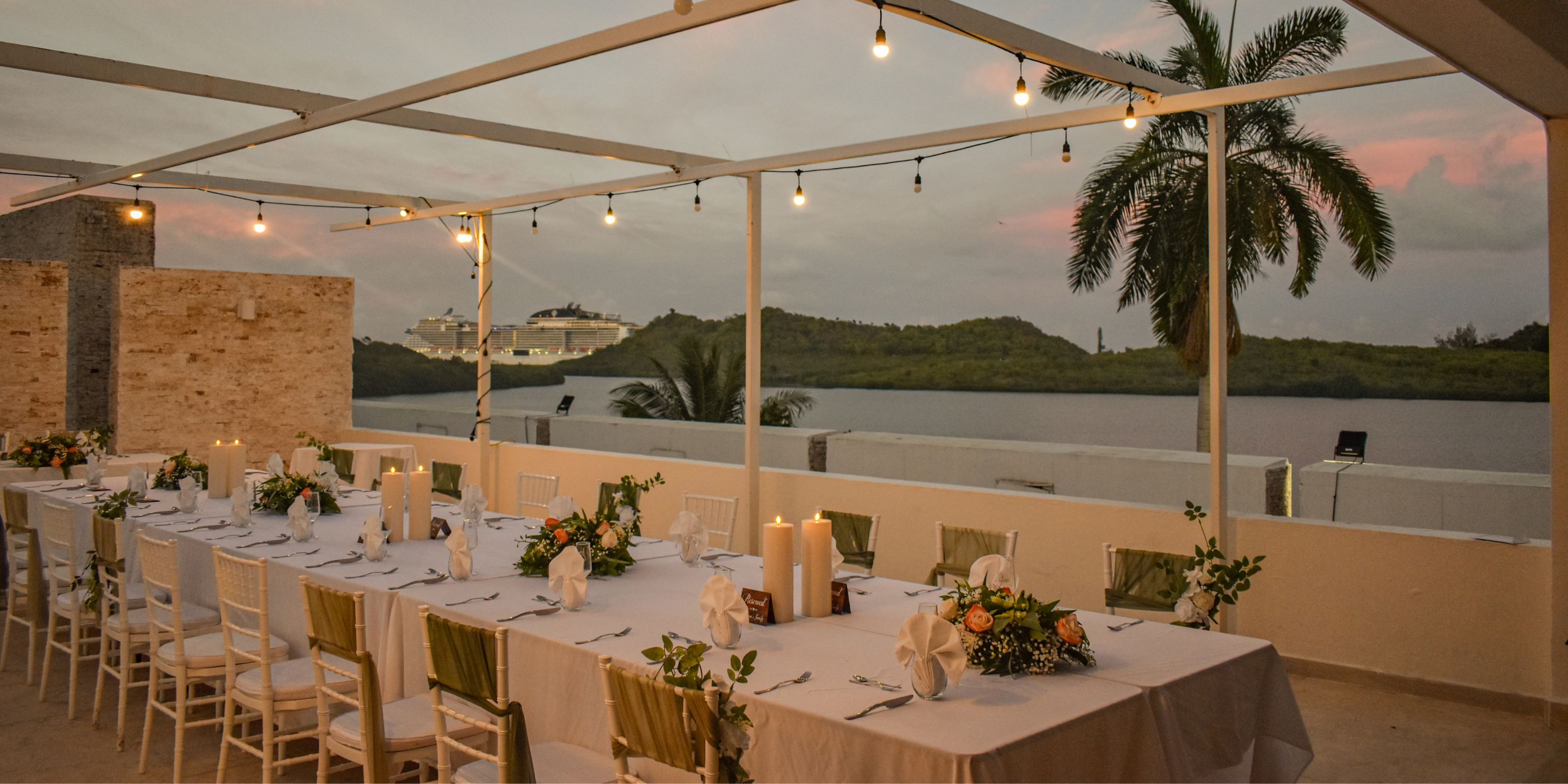 Destination wedding setup with long tables for outdoor dining at Royalton Antigua, sunset over the water.