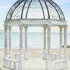 White gazebo on a beach with palm trees against an ocean backdrop, perfect for destination weddings during sunset.