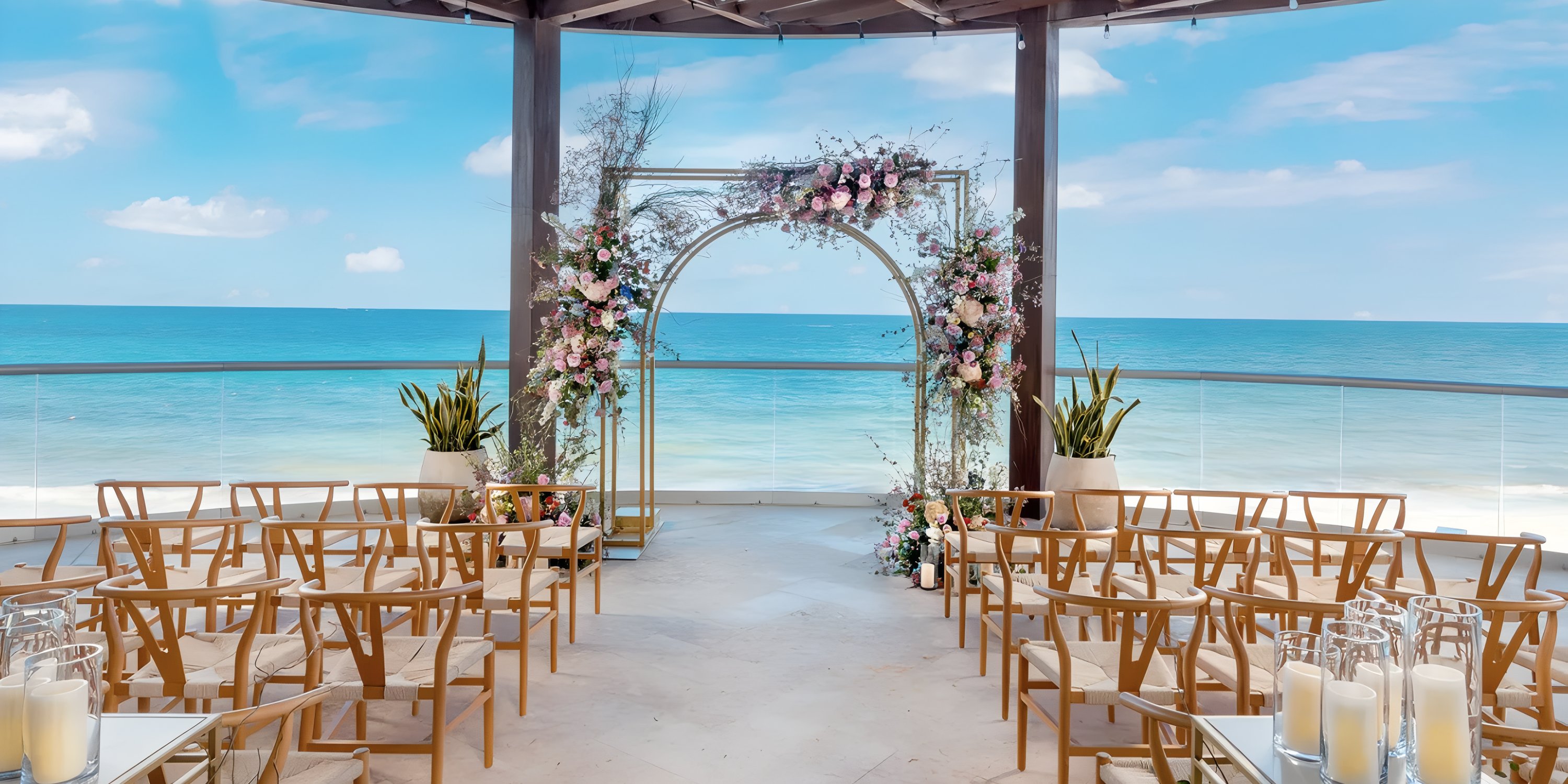 Destination wedding ceremony setup with floral arch and rows of chairs by the ocean at Sun Palace gazebo.