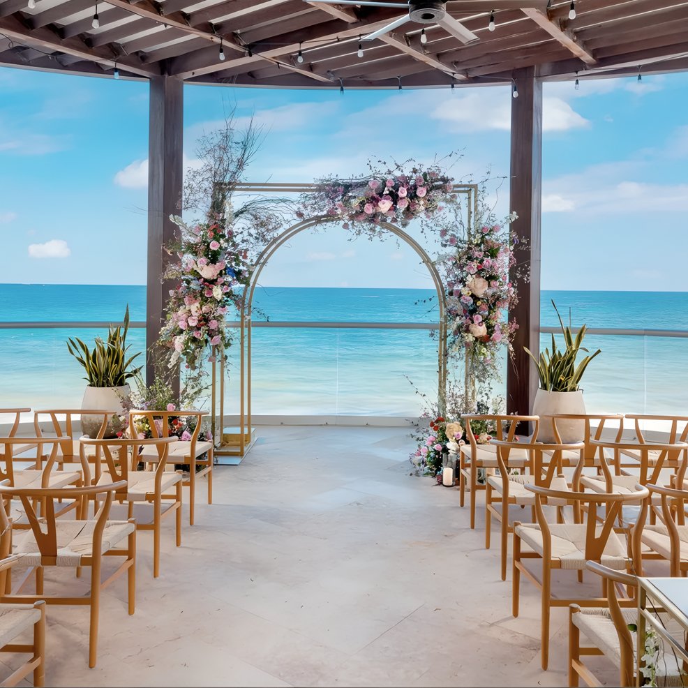 Destination wedding ceremony setup featuring a floral arch, wooden chairs, and a scenic ocean backdrop.
