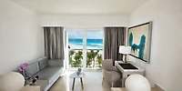 Elegant modern room at Le Blanc Spa Resort, perfect for a destination wedding, featuring breathtaking views of the ocean, palm trees, and beach through expansive windows.