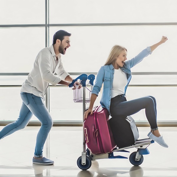 A happy couple at the airport with a WorldCarte Smarte Carte airport luggage cart planning airfare for destination wedding