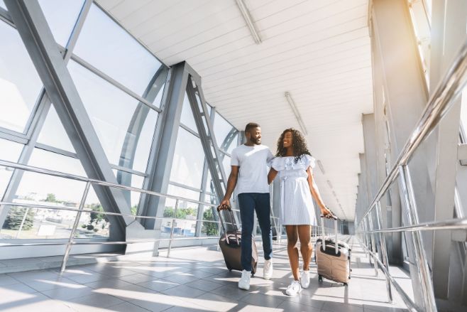 A black couple walk their rolling luggage along an aisle what we recommend airfare