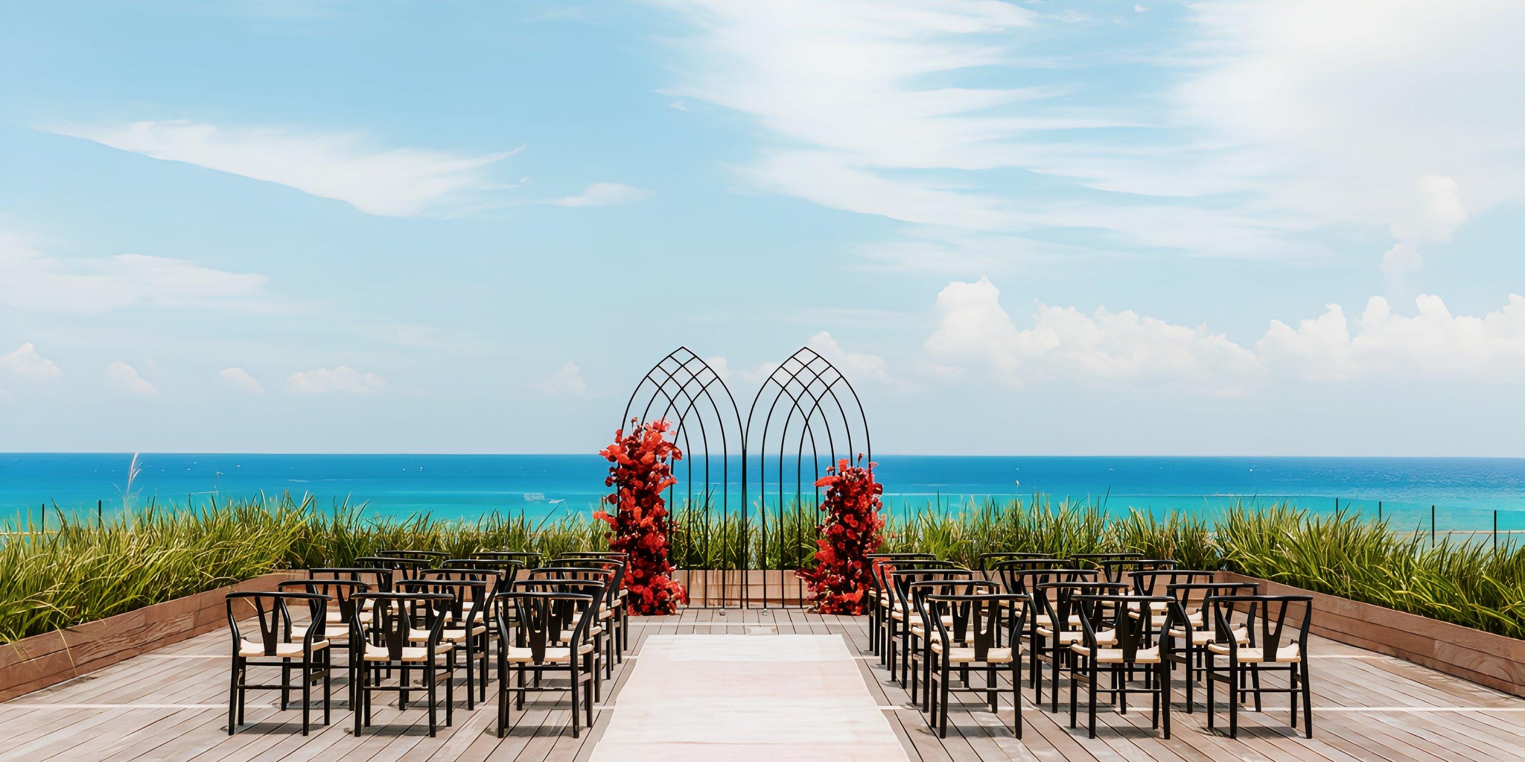 Chairs arranged for a destination wedding face a floral arch on an oceanfront deck at Secrets Moxche.