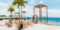 Destination wedding setup at Secrets Moxche: deck with chairs, floral arch, palms, and ocean backdrop.