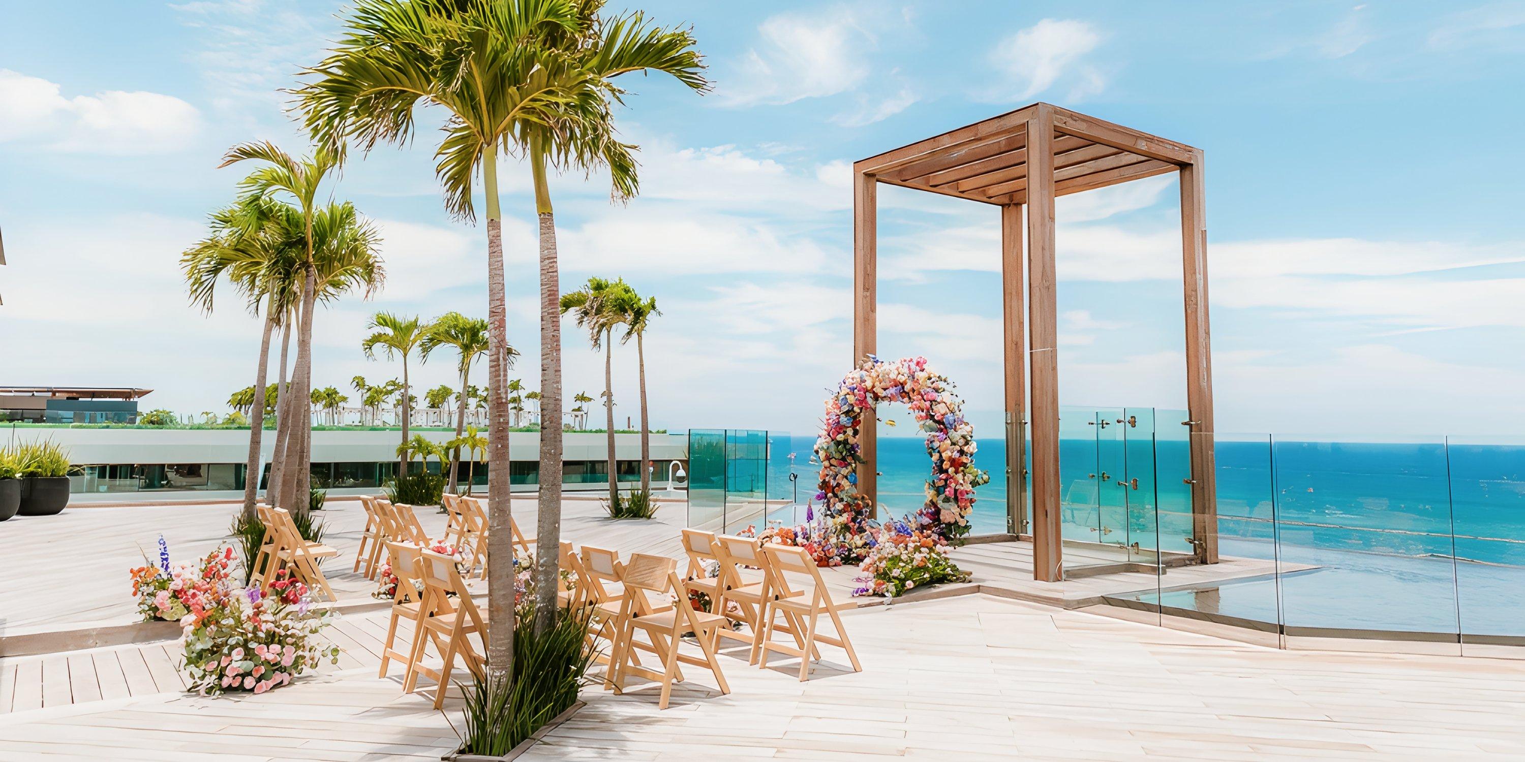 Destination wedding setup at Secrets Moxche: deck with chairs, floral arch, palms, and ocean backdrop.