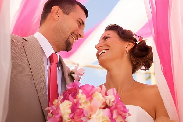 Smiling bride and groom at their destination wedding under pink and white fabric at Breezes Resort Bahamas.