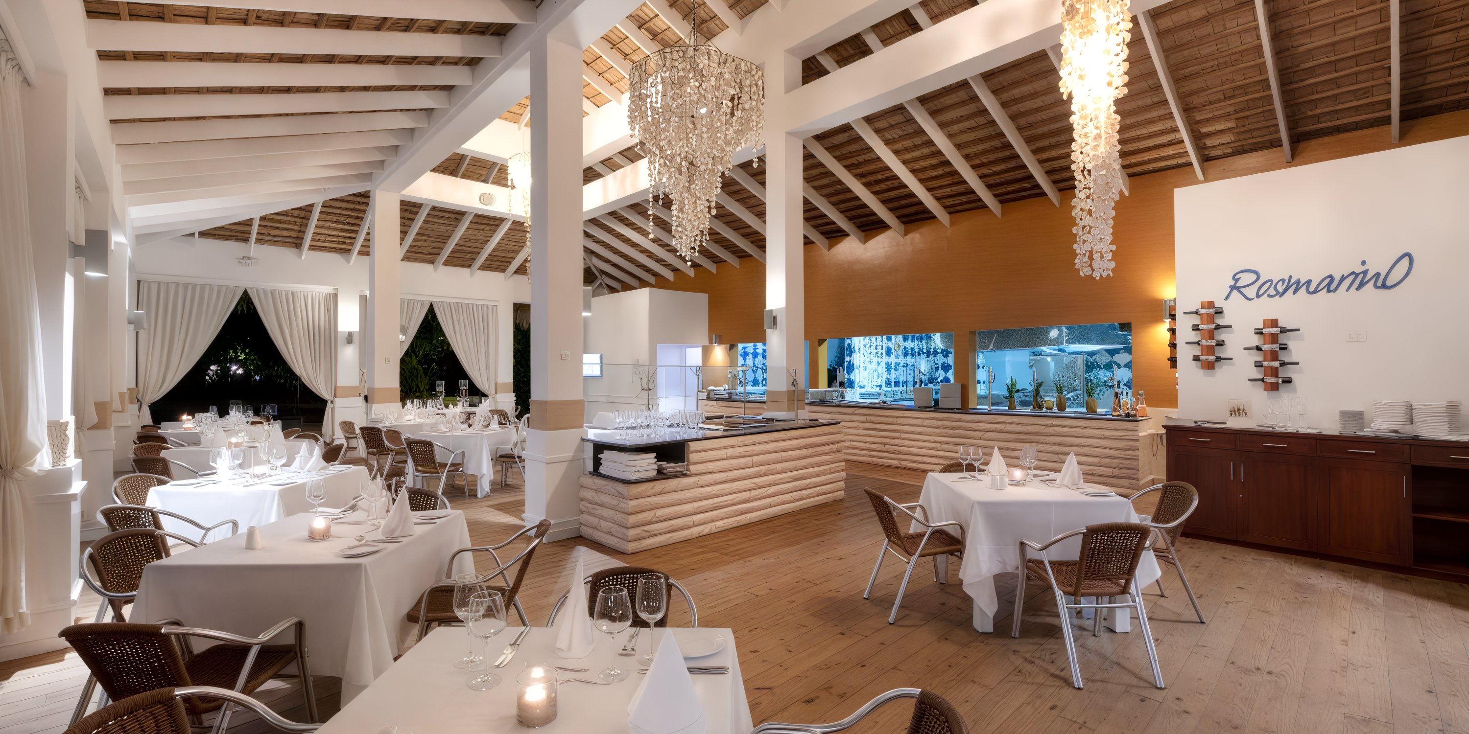 The elegant restaurant interior exudes a wedding-worthy charm, featuring white tablecloths, wicker chairs, and dazzling crystal chandeliers. Perfect for a destination wedding celebration or an intimate reception.