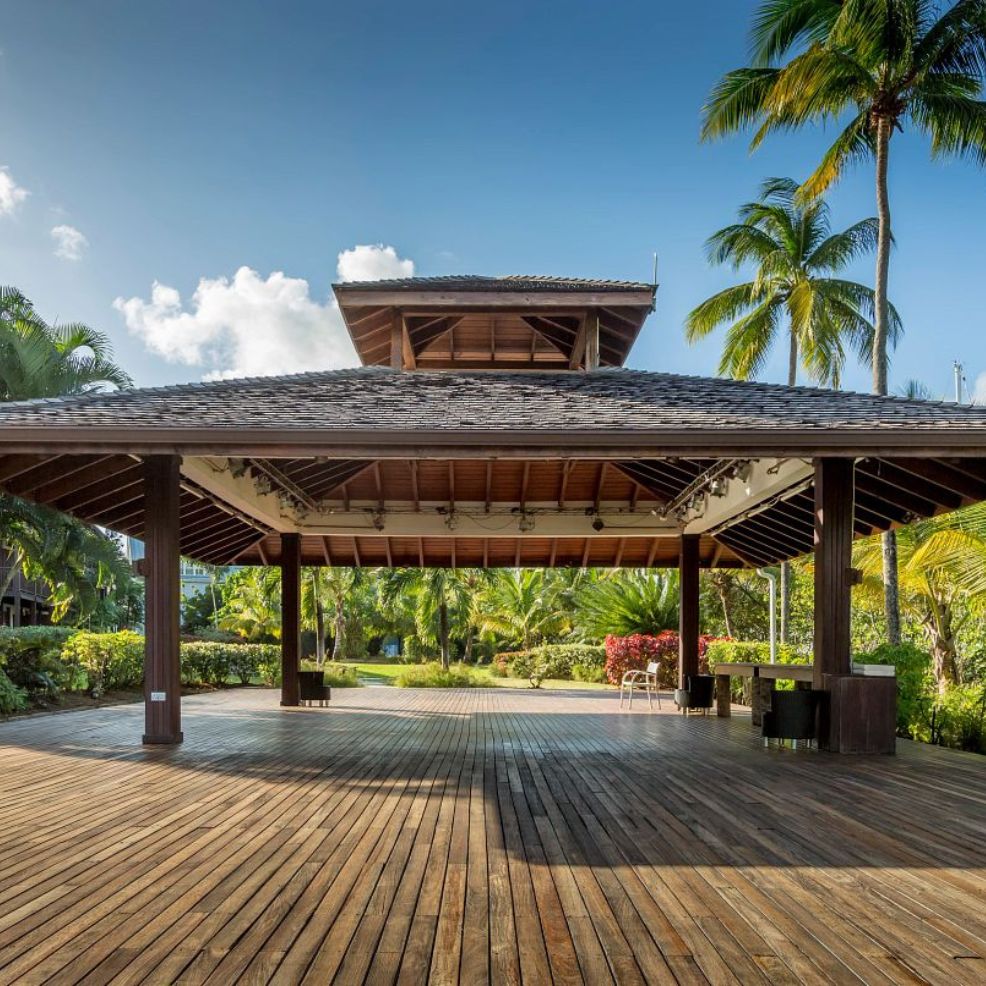 Open wooden pavilion with a peaked roof, ideal for a destination wedding, amid palm trees and greenery.