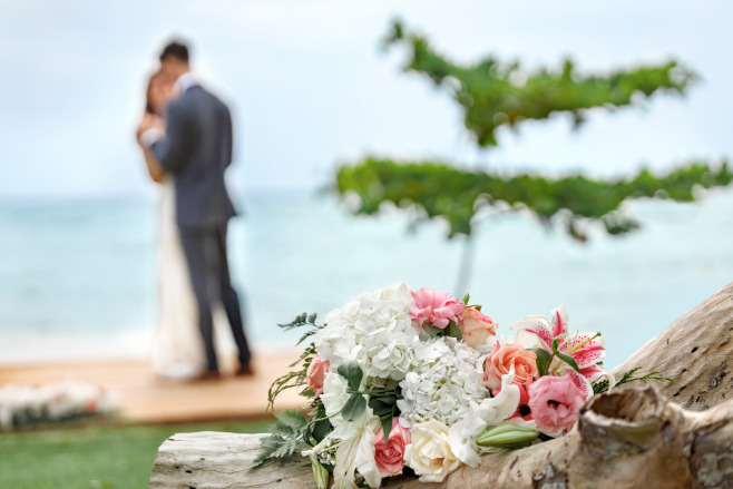 A bouqet in the foreground of a couple kissing after their cheap Cancun wedding package destination wedding