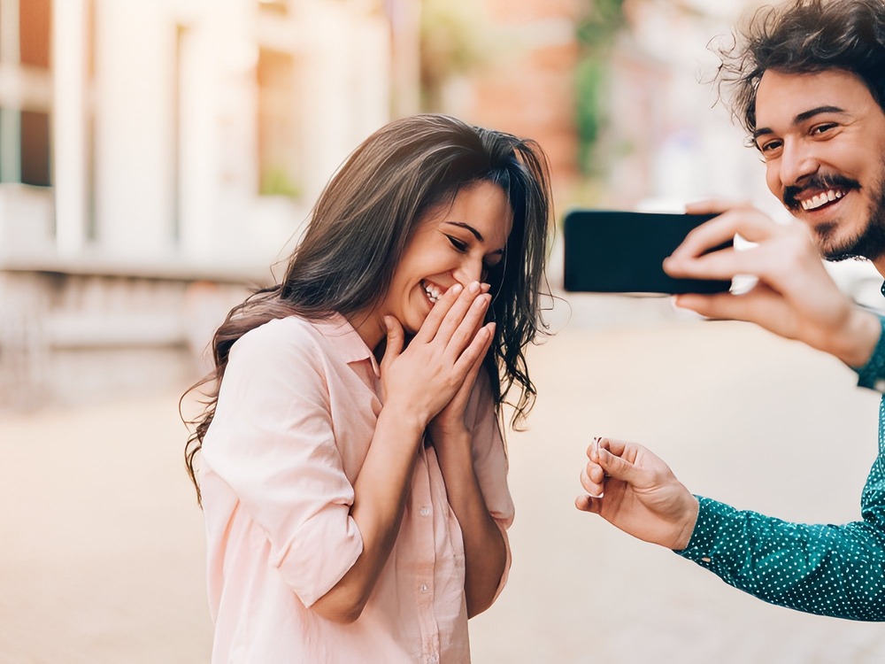 A man proposes to a smiling woman outdoors—one of the best wedding proposal moments captured on camera, perfect for inspiring your own destination wedding.