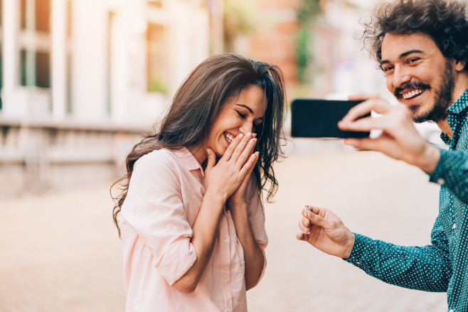 A man photographs his girlfriend saying 'yes' to his proposal