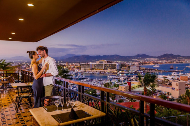 Couple kissing on the balcony with Sandos Finisterra Los Cabos in the distance