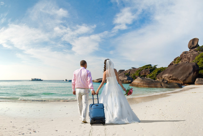 A bride and groom pull their luggage on the white sand beaches of the Caribbean