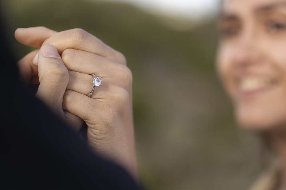 Close-up of a hand adorned with a lab-grown diamond wedding ring, gently holding another person's hand during an outdoor destination wedding.