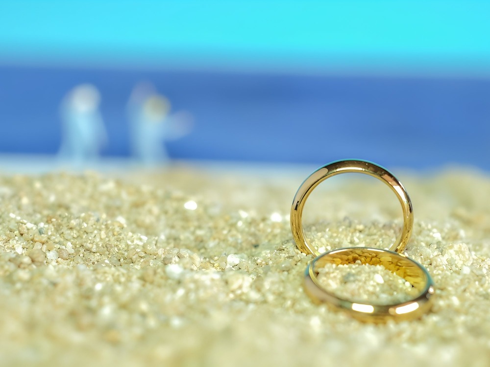 Two gold wedding rings rest on a sandy beach—perfect inspiration for romantic wedding or destination wedding proposal ideas.