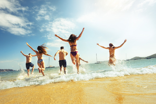 A group of young people run through the waves on a beach