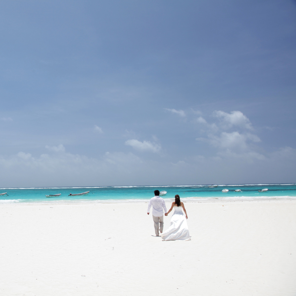 A couple standing hand in hand on a beach after their big day at a Playa destination wedding resort