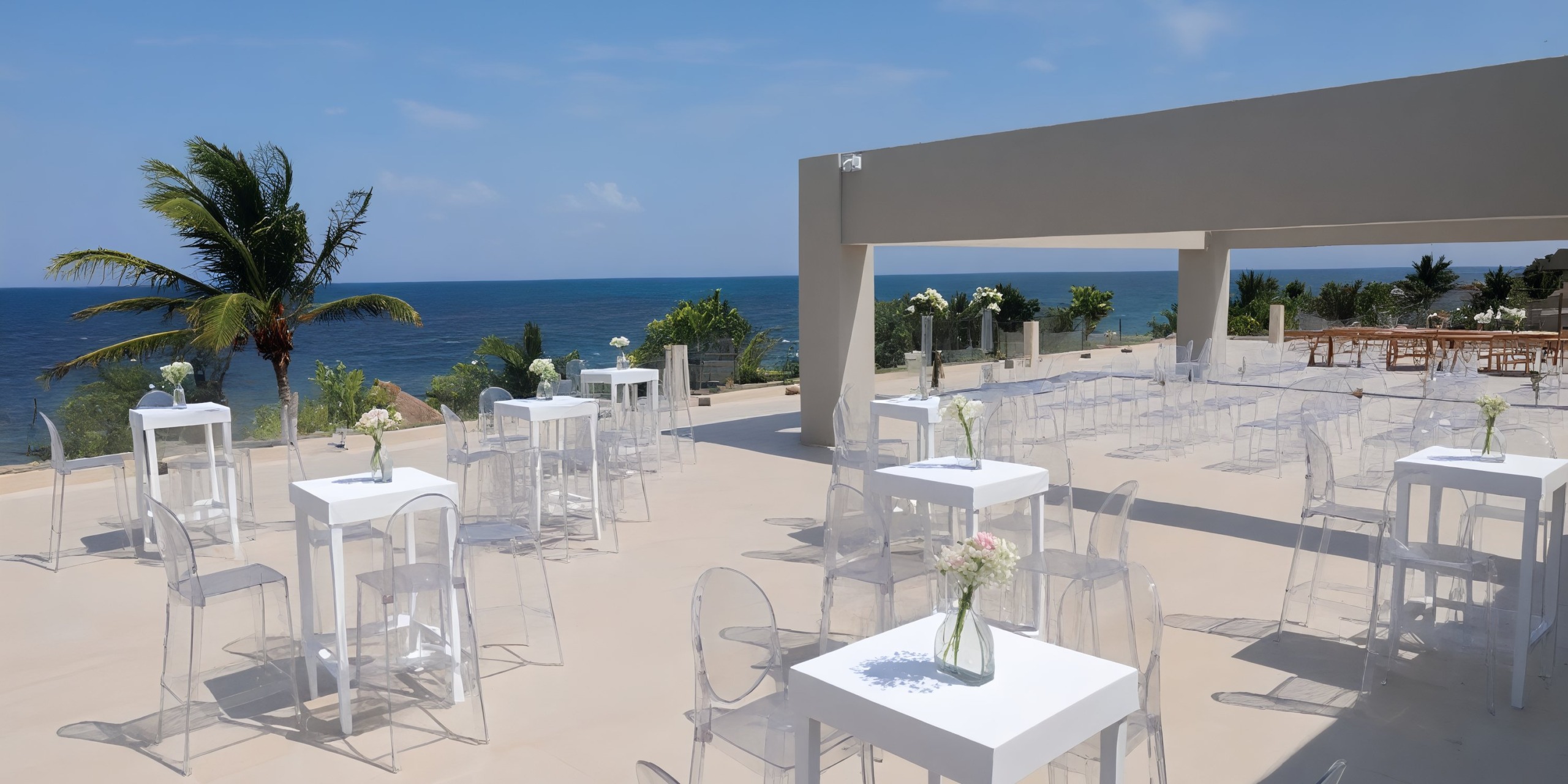 The patio at Royalton Splash Riviera Cancun, featuring clear chairs and white tables, provides a stunning ocean view that is perfect for a destination wedding.