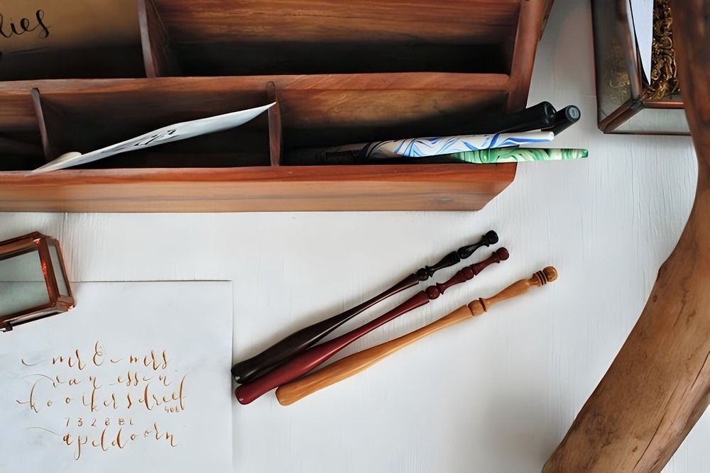 Wooden desk organizer filled with pens, calligraphy paper, and elegant destination wedding invitations.