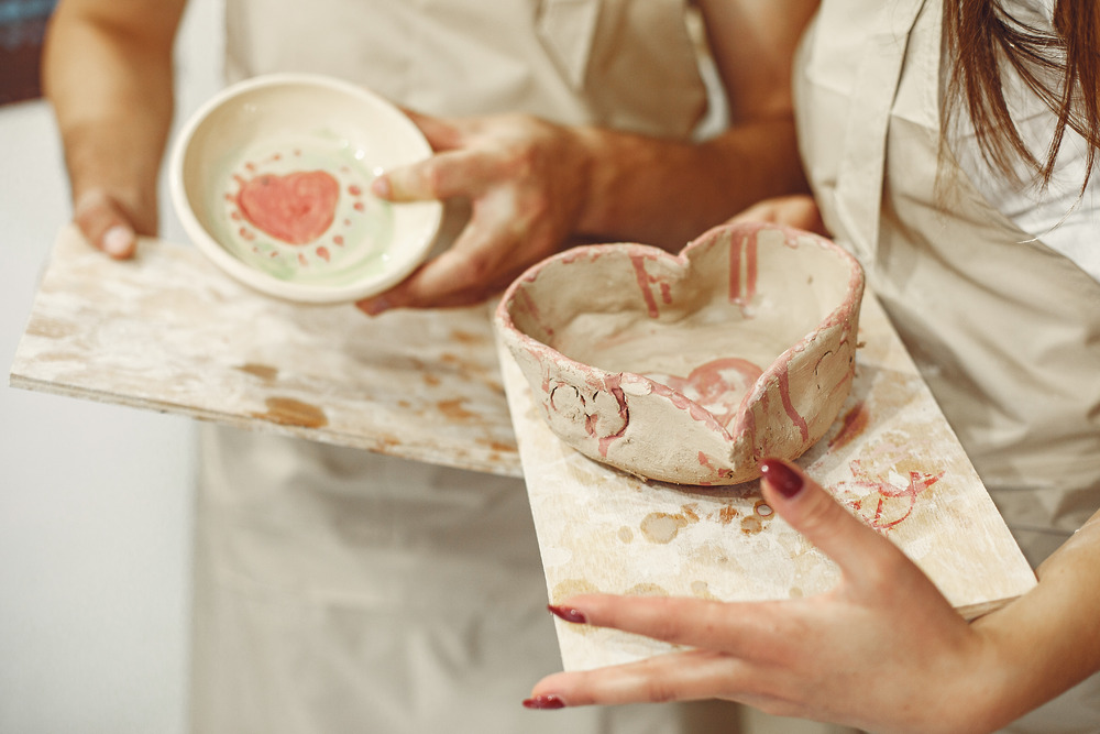Two people hold handmade ceramic bowls adorned with heart designs—thoughtful destination wedding favors that add a unique touch to the celebration.