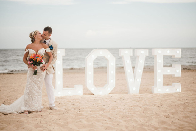 Couple kissing on the beach with massive letters spelling 'Love'