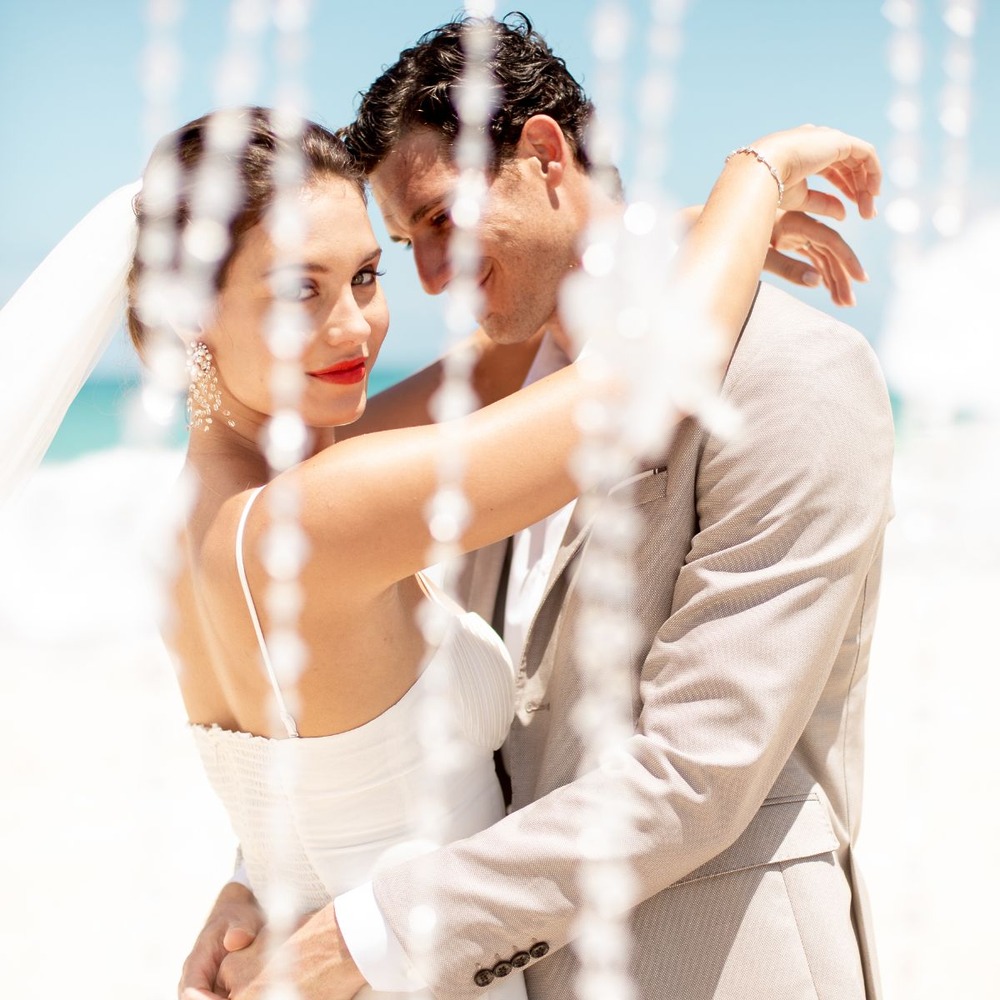 A bride and groom share an embrace on a sunlit beach, exemplifying the magic and romance that comes with a destination wedding, all while reflecting the typical cost of such a celebration.