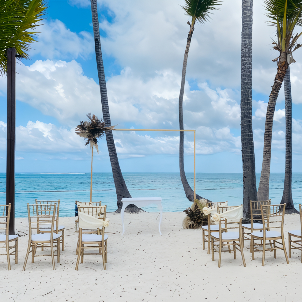 Empty chairs on the sandy beach face a wedding arch by the sea, perfect for a destination wedding.