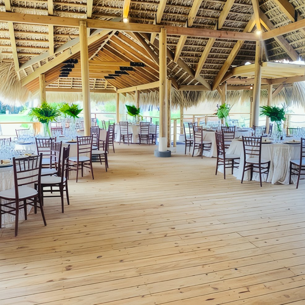 Open-air pavilion with wooden floors, round tables, chairs, and green centerpieces for a wedding.