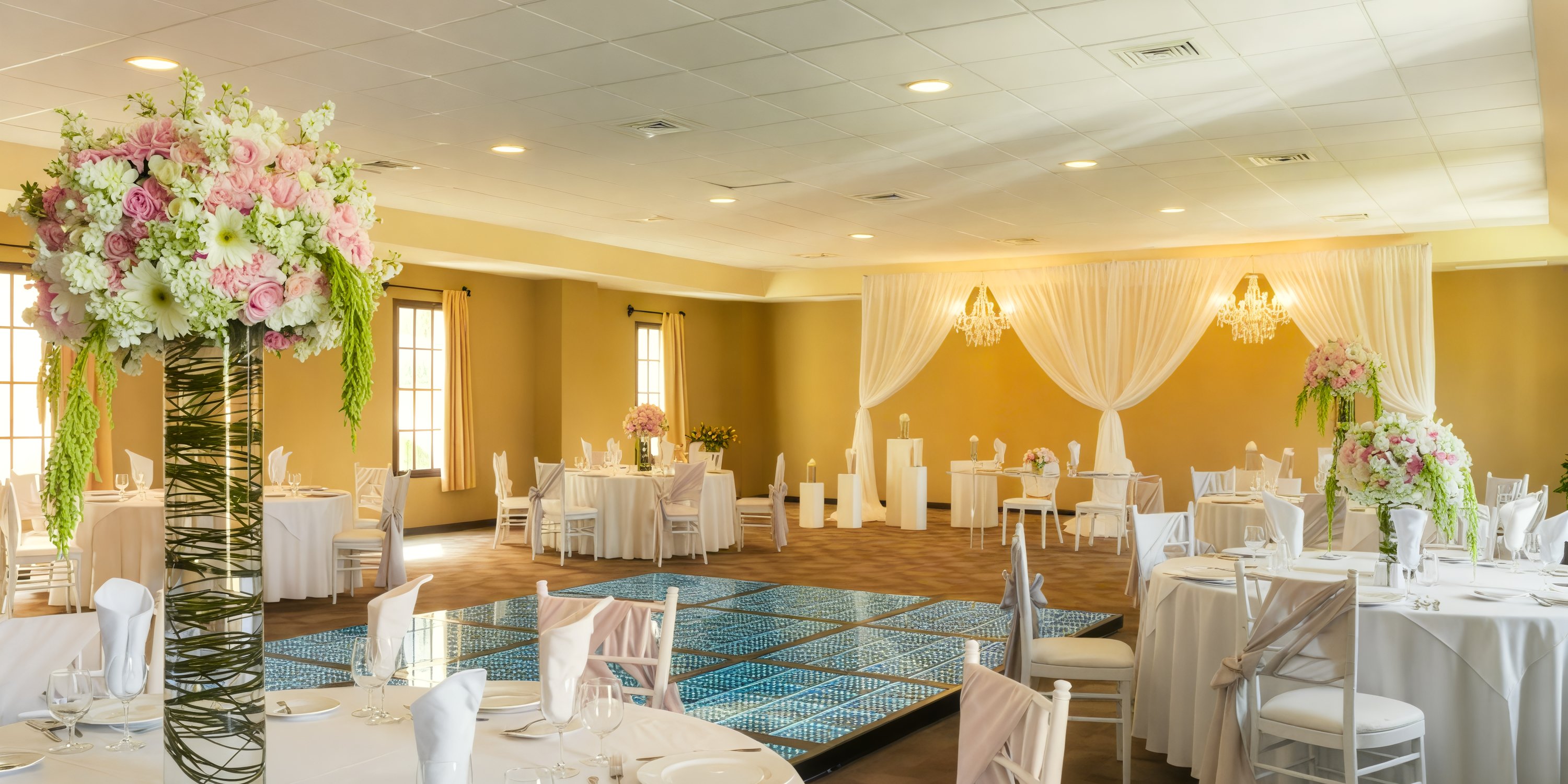 Ocean Coral Spring: Experience the elegance of a destination wedding in a stunning hall adorned with floral centerpieces, round tables, and a beautifully draped backdrop.