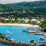 Tropical coastal resort in Jamaica tourism zone with white sandy beach, moored yachts, turquoise water, and lush green hills in the background.