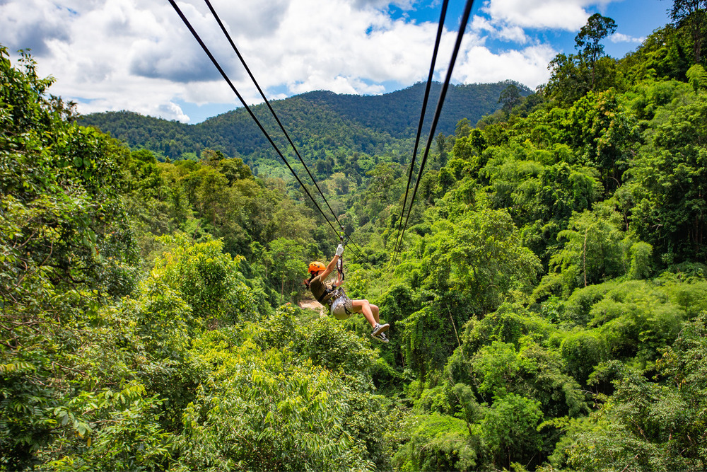 Woman ziplining in the jungles behind a mountain