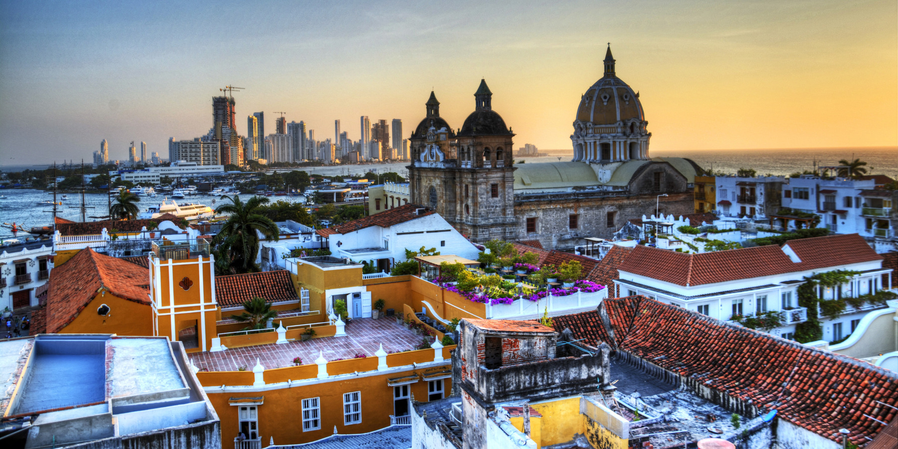Sunset view of Cartagena, Colombia showing historic architecture with domed rooftops in the foreground and modern skyscrapers in the distance, popular for destination weddings.