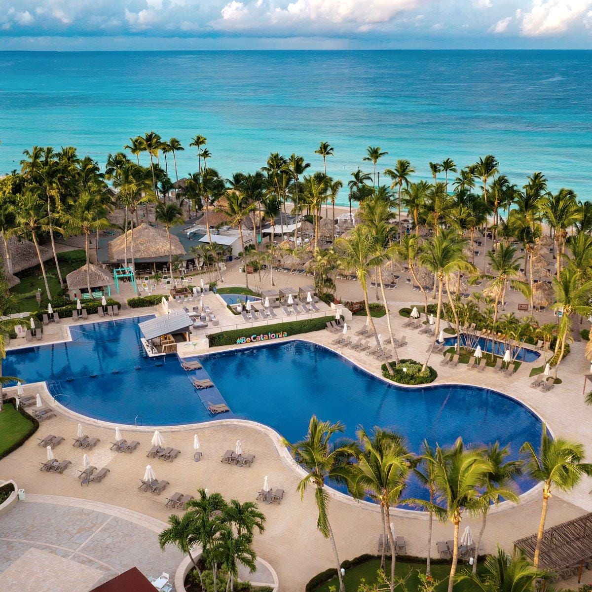 Aerial view of a beachfront resort, ideal for a destination wedding, with large pool, palms, and lounge chairs.
