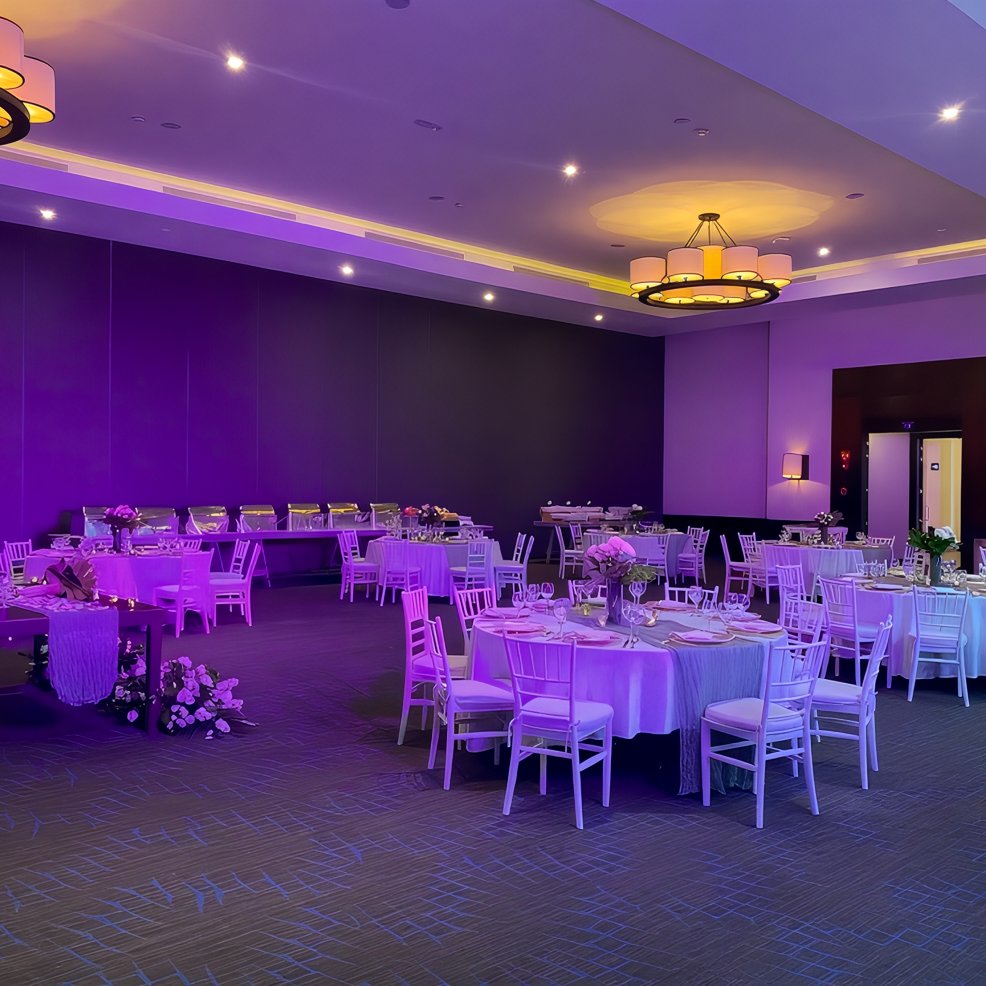 Ballroom set for a destination wedding, featuring round tables, white chairs, and purple lighting.